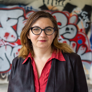 Portrait of CoED Inna Michaeli smiling. Behind them is a wall with grafiti.